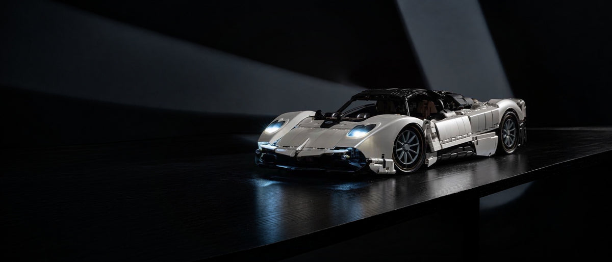 White brick-built hypercar model with glowing headlights on a dark table under soft beams of light
